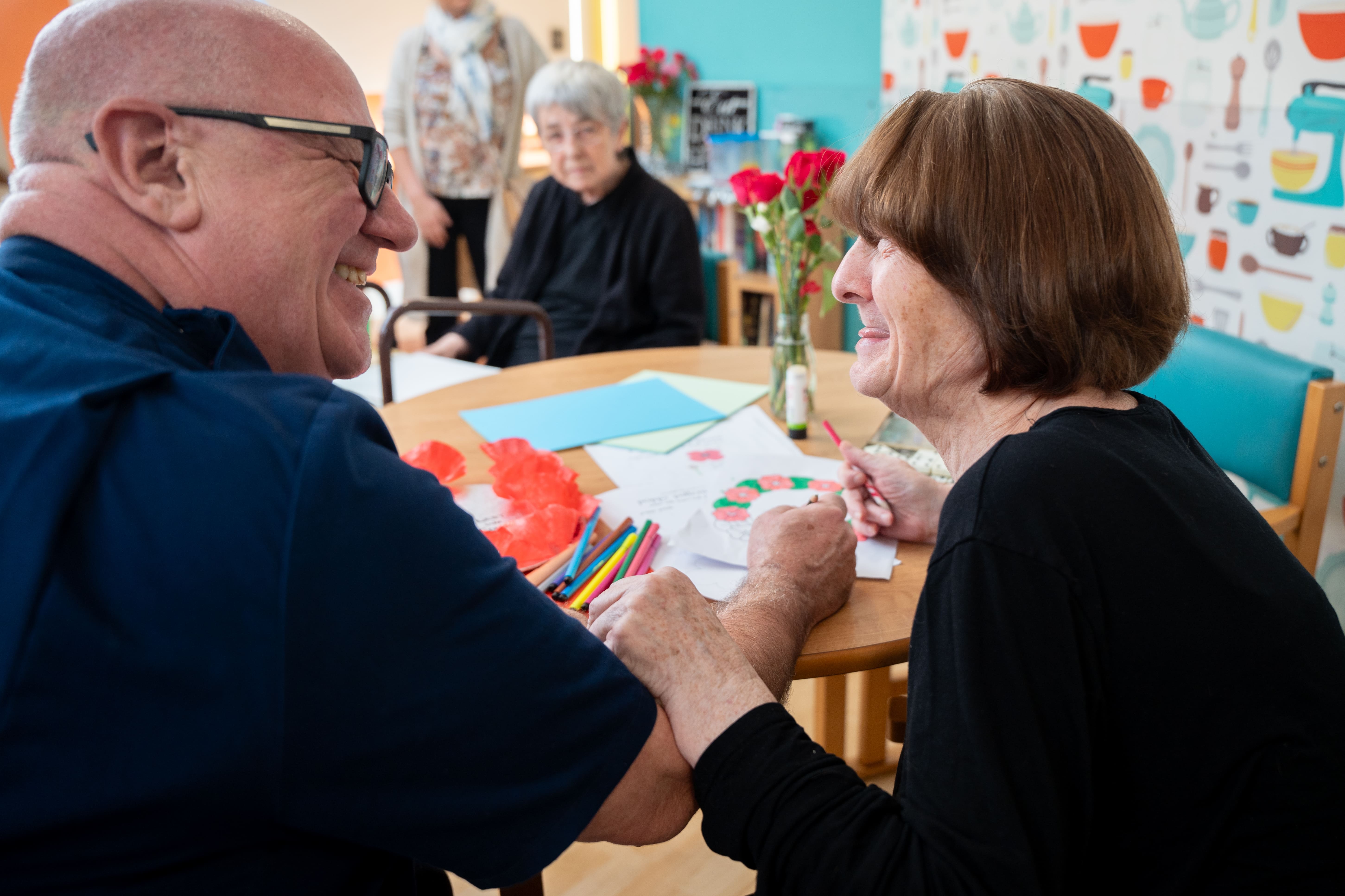 Residents at Southbourne Care Home smile and chat while making flower crafts together around a table during a creative activity session.