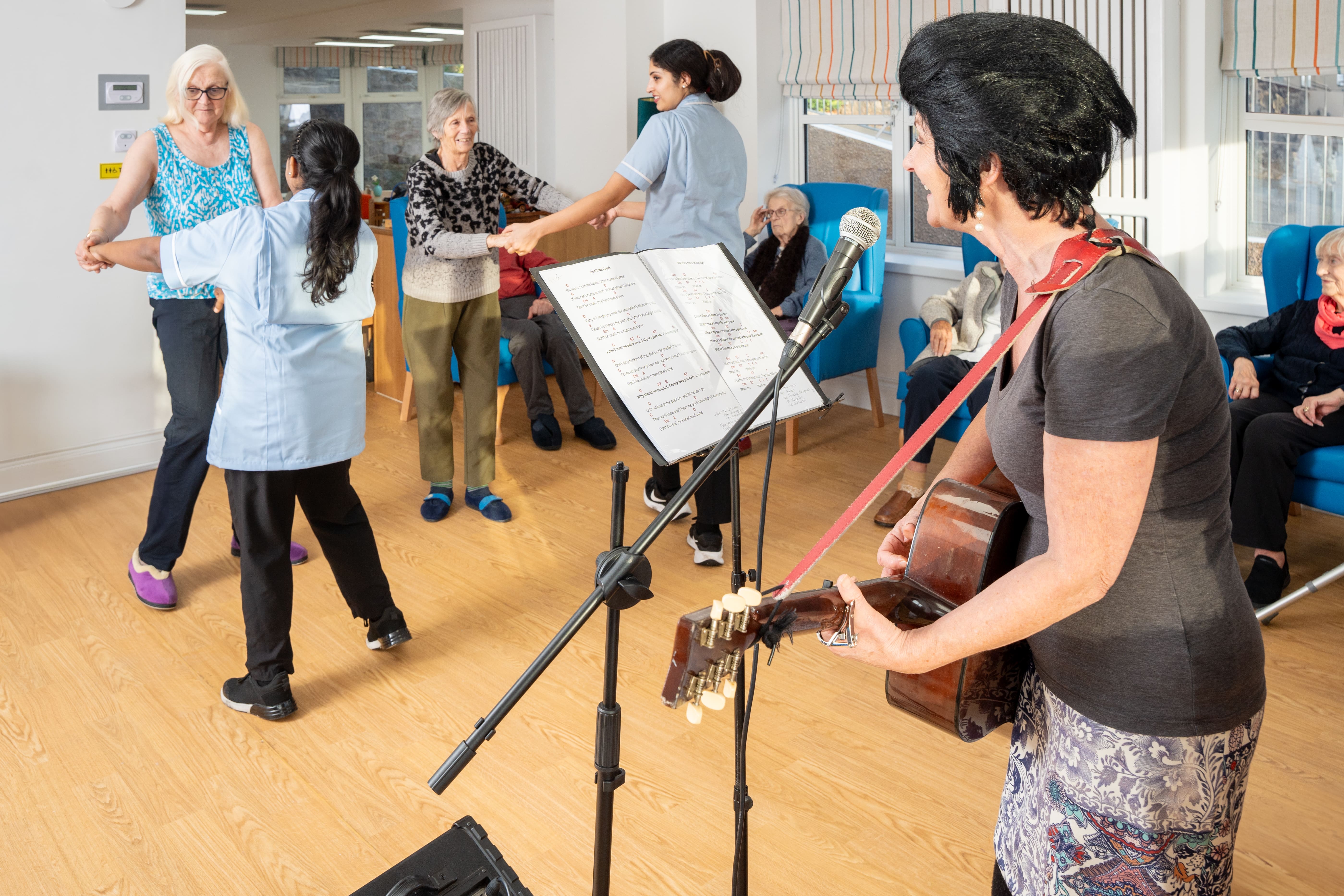 Residents at Cary Lodge Care Home in Babbacombe enjoy live music and gentle dancing with staff support during a group activity session.