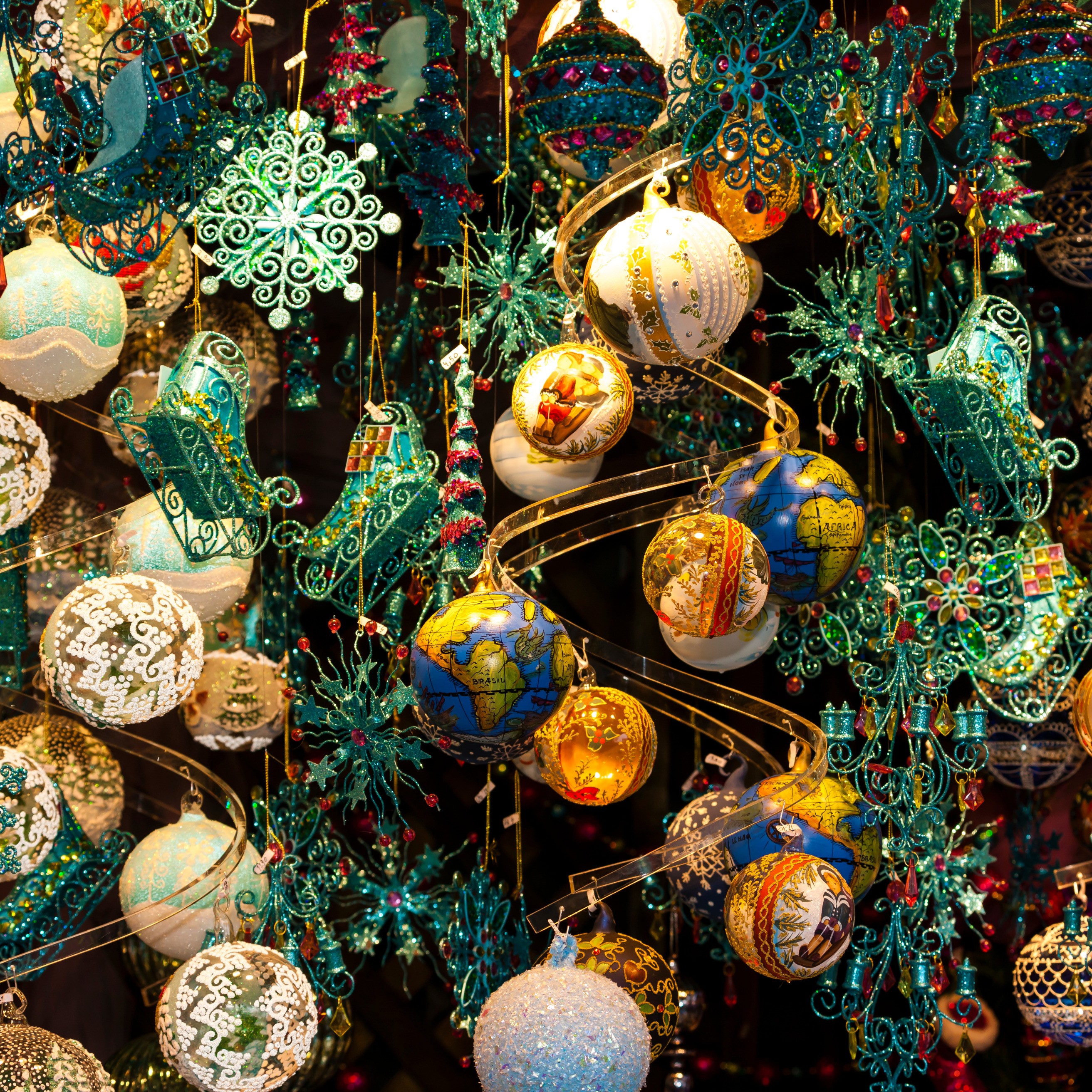 A vibrant display of colorful Christmas ornaments, including globes, glittery baubles, sleighs, and snowflakes, hanging in festive abundance.