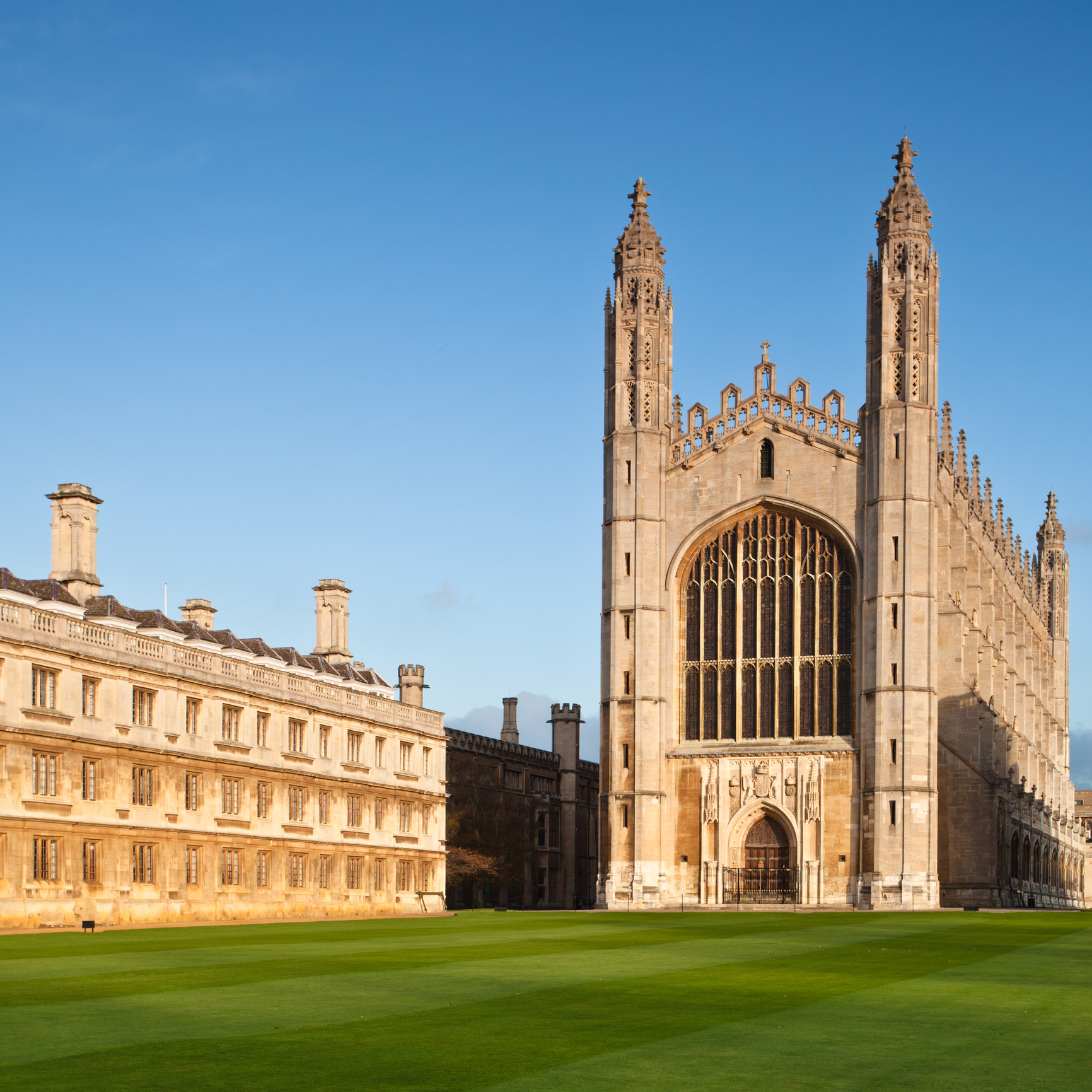 Sunlit view of King&rsquo;s College Chapel, Cambridge, showcasing its iconic Gothic architecture against a clear blue sky.