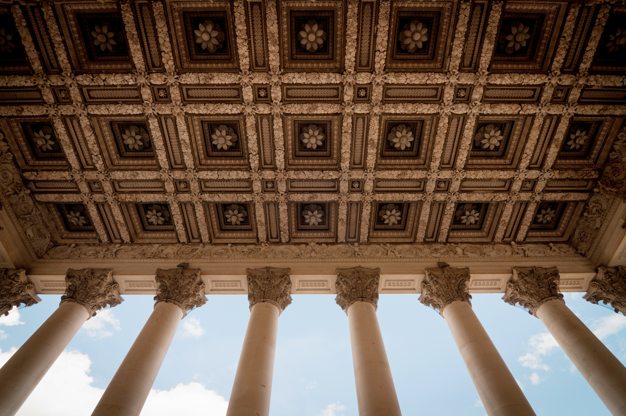 Ornate coffered ceiling and classical columns at the Fitzwilliam Museum in Cambridge, viewed from below against a blue sky.
