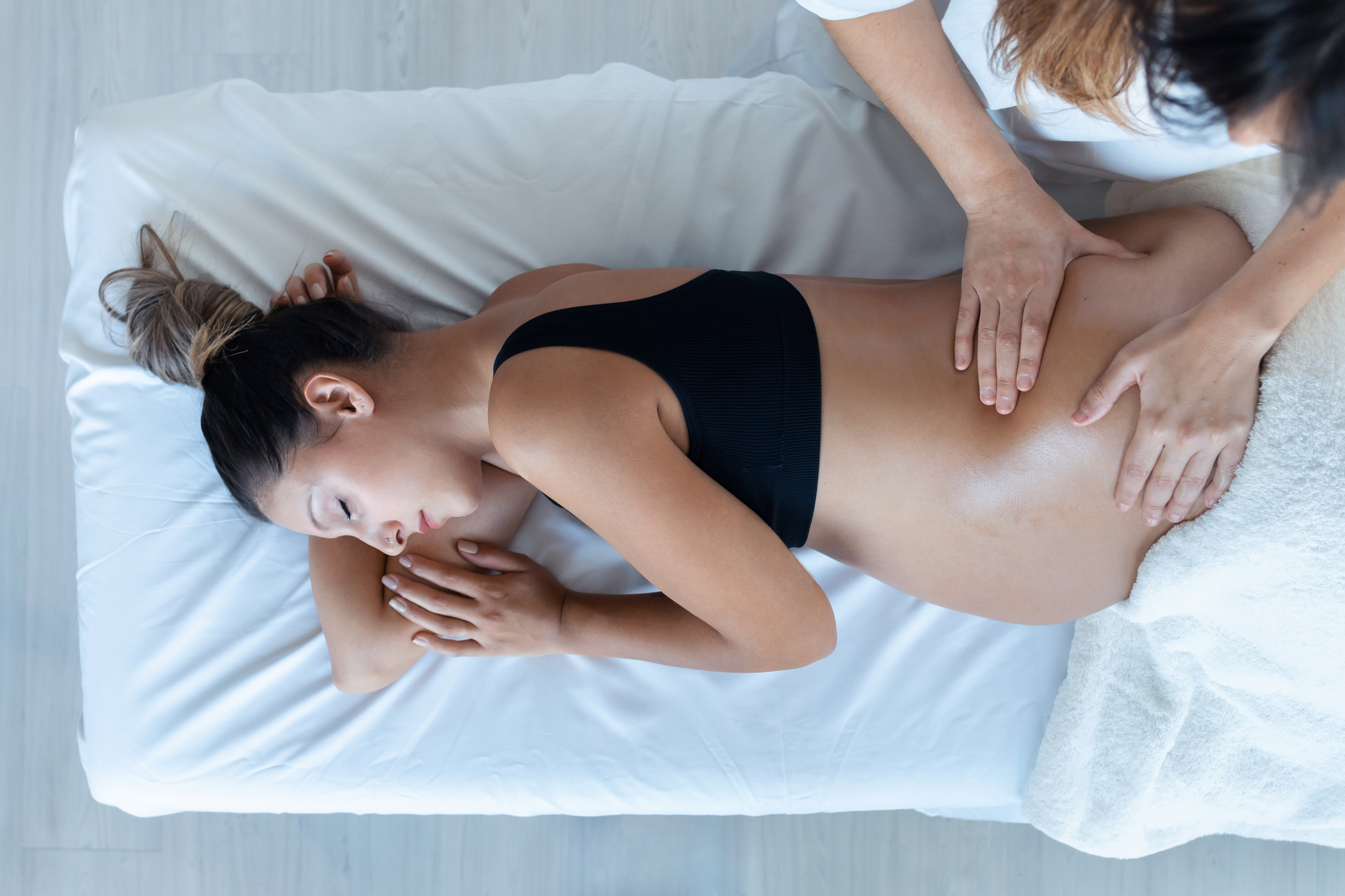 Side view of a relaxed pregnant woman getting a prenatal massage on a white-sheeted table.