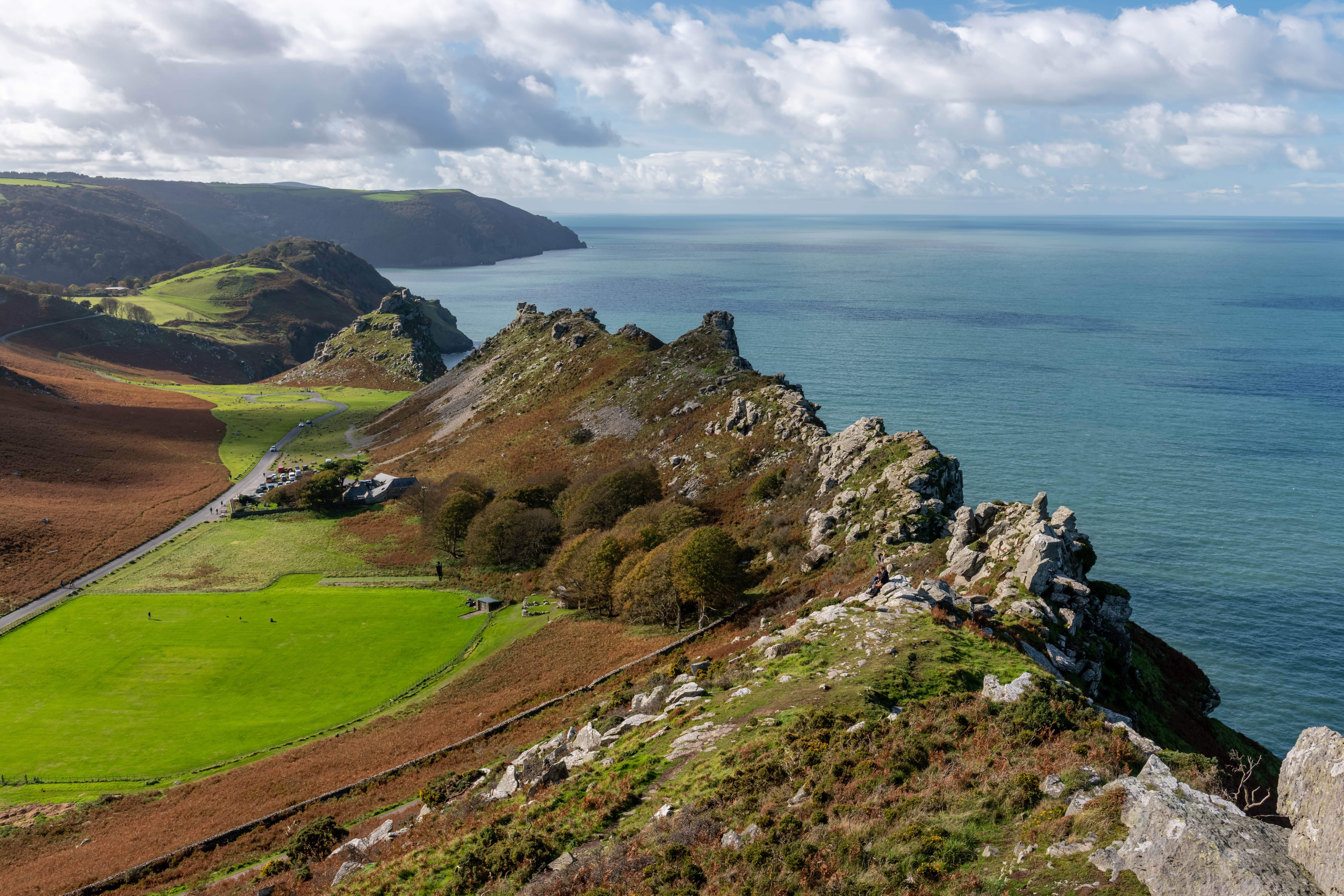 Scenic view of the Valley of the Rocks in North Devon, with dramatic rocky ridges, green fields, and cliffs overlooking the calm blue sea under a partly cloudy sky.