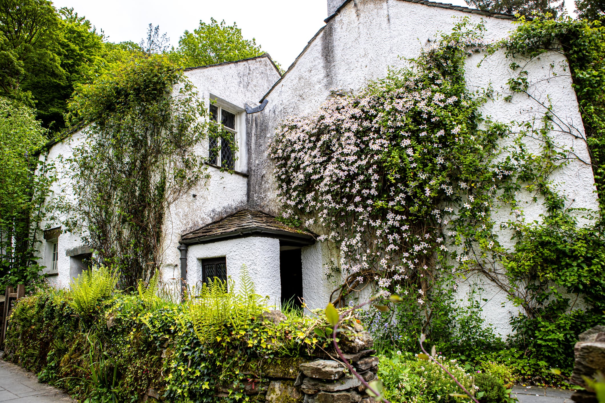 Dove Cottage, former home of poet William Wordsworth, with whitewashed walls, flowering vines, and a lush garden in the Lake District countryside.