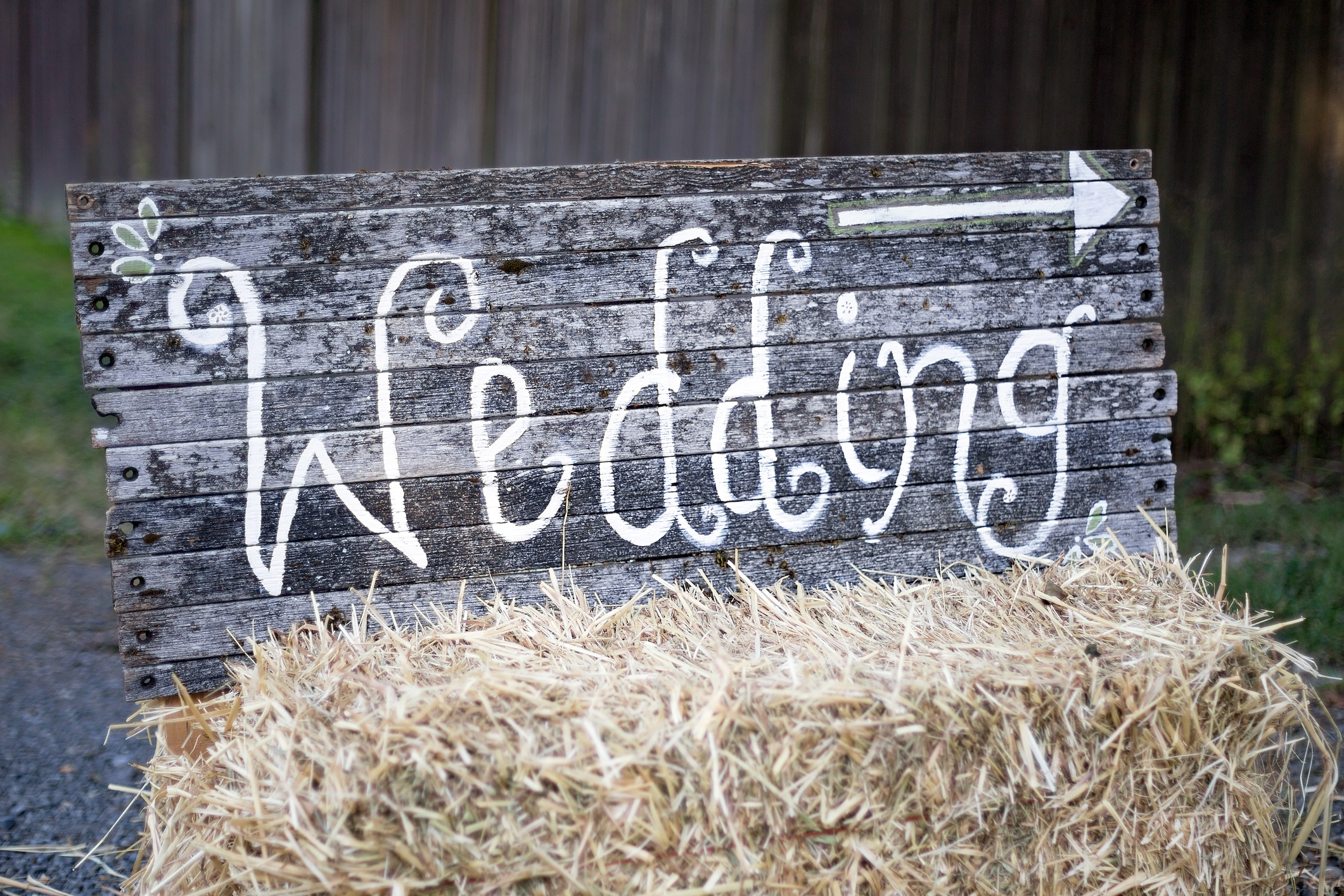 Rustic wooden sign reading &ldquo;Wedding&rdquo; with a right-pointing arrow, propped on a hay bale outdoors.