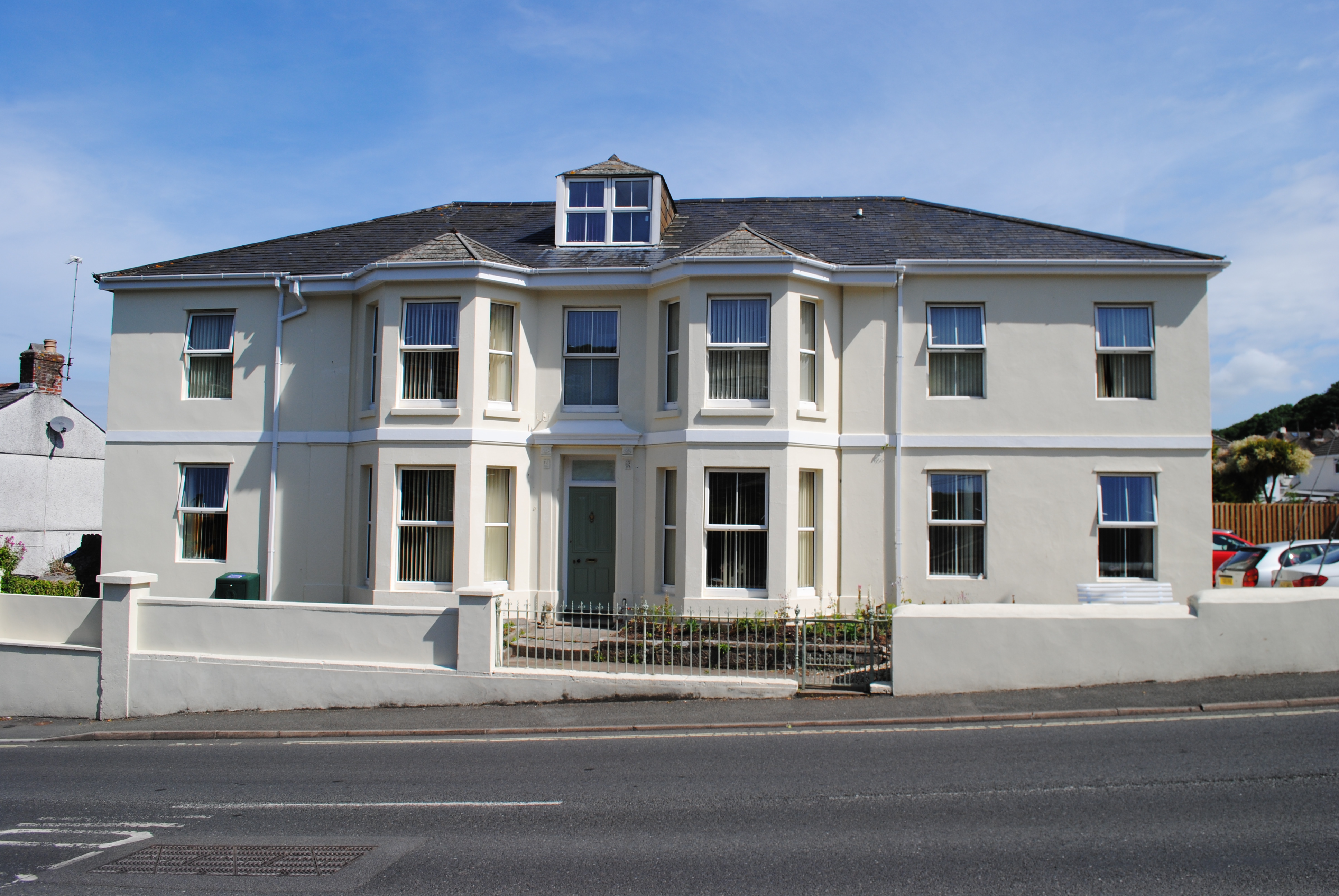 Front view of Wisteria House Plymstock, a cream-coloured, two-storey building with large windows, set against a clear blue sky.
